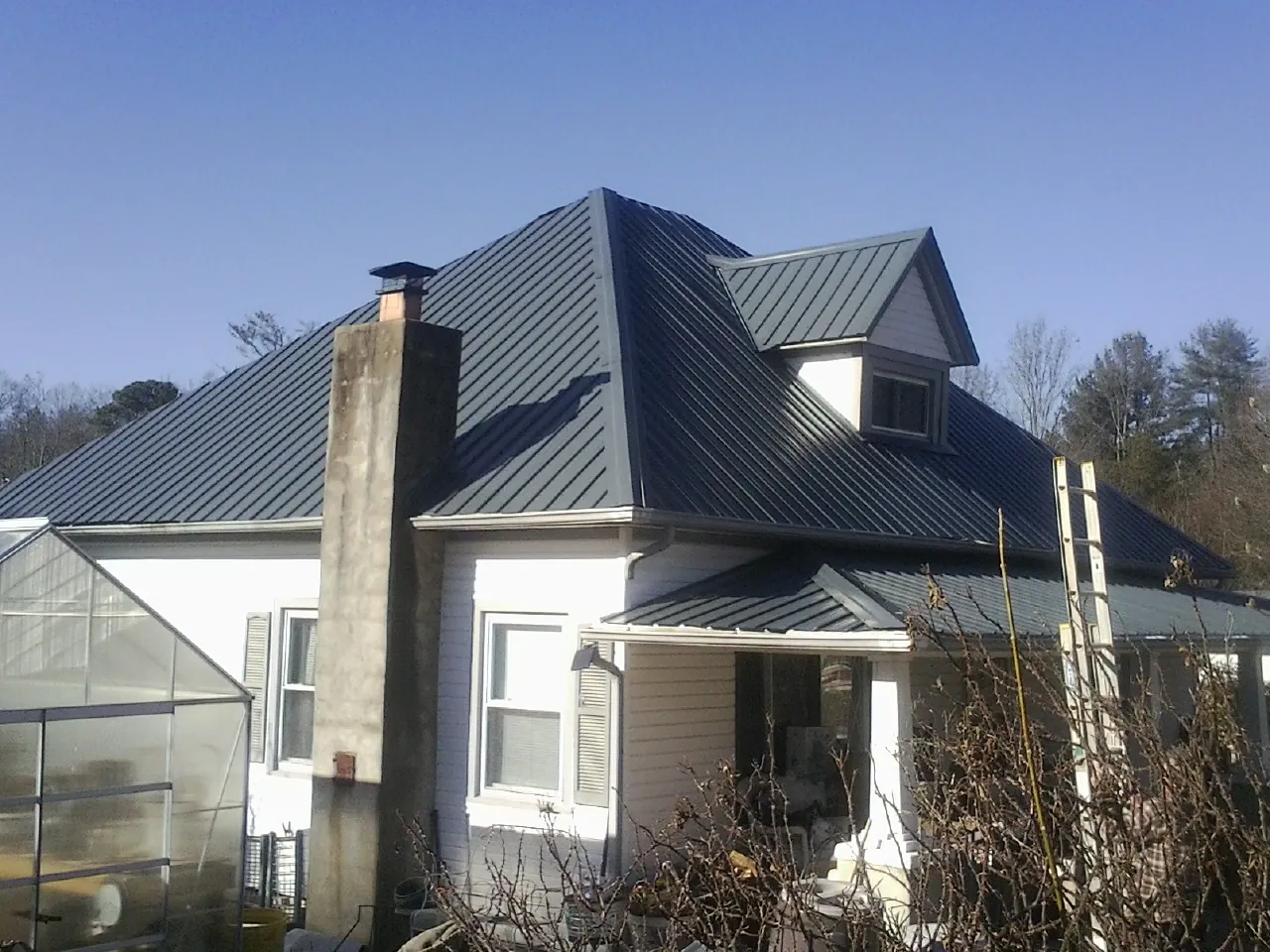 Dark blue standing seam metal roof on a white farmhouse with dormer — Slate & Tile Roof Repair by Roofing Brothers in Truesdale