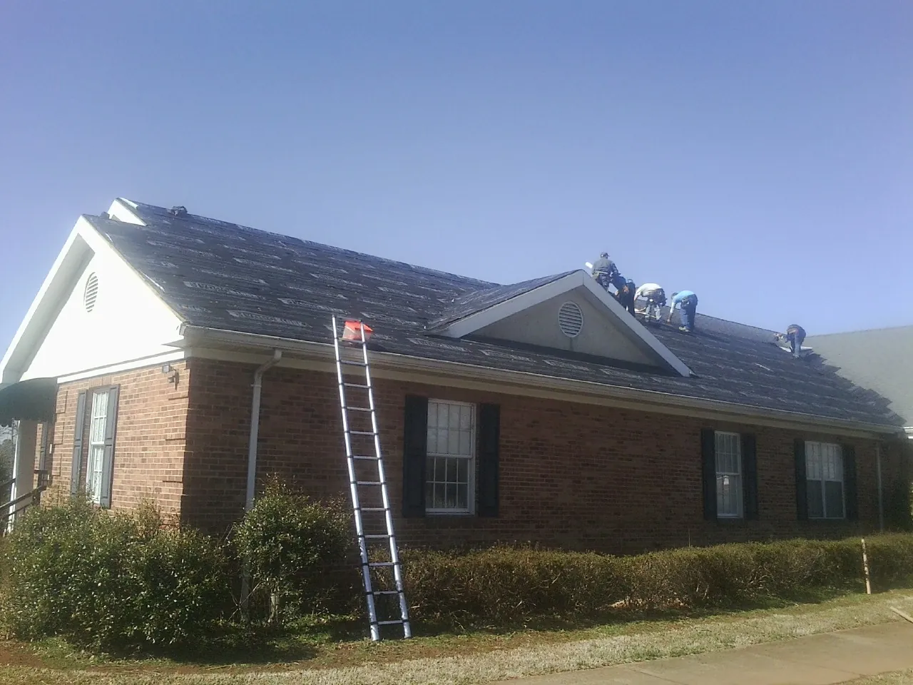 Crew tearing shingles off a brick ranch roof with a ladder set — Emergency Roof Repair work by our crew in Truesdale