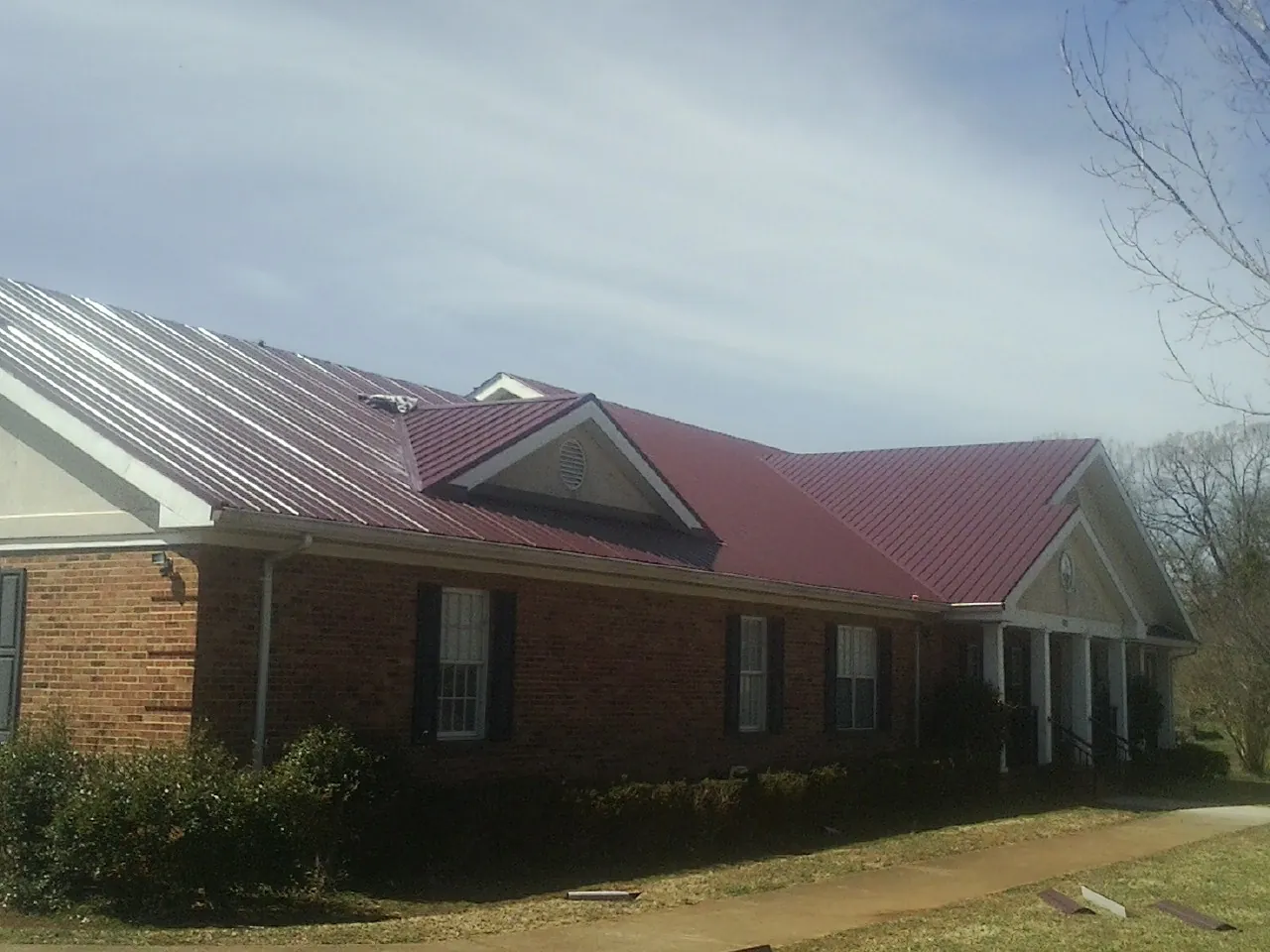 Red metal roof with gabled entries on a long brick building, from a Hail Damage Roof Repair job in Truesdale