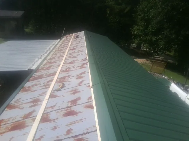 Old rusted panels beside newly installed green metal roofing — Wind Damage Roof Repair by Roofing Brothers in Truesdale
