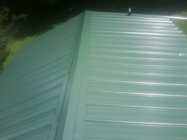 New green metal panels meeting at the ridge of a roof — Flat Roof Repair work by our crew in Truesdale