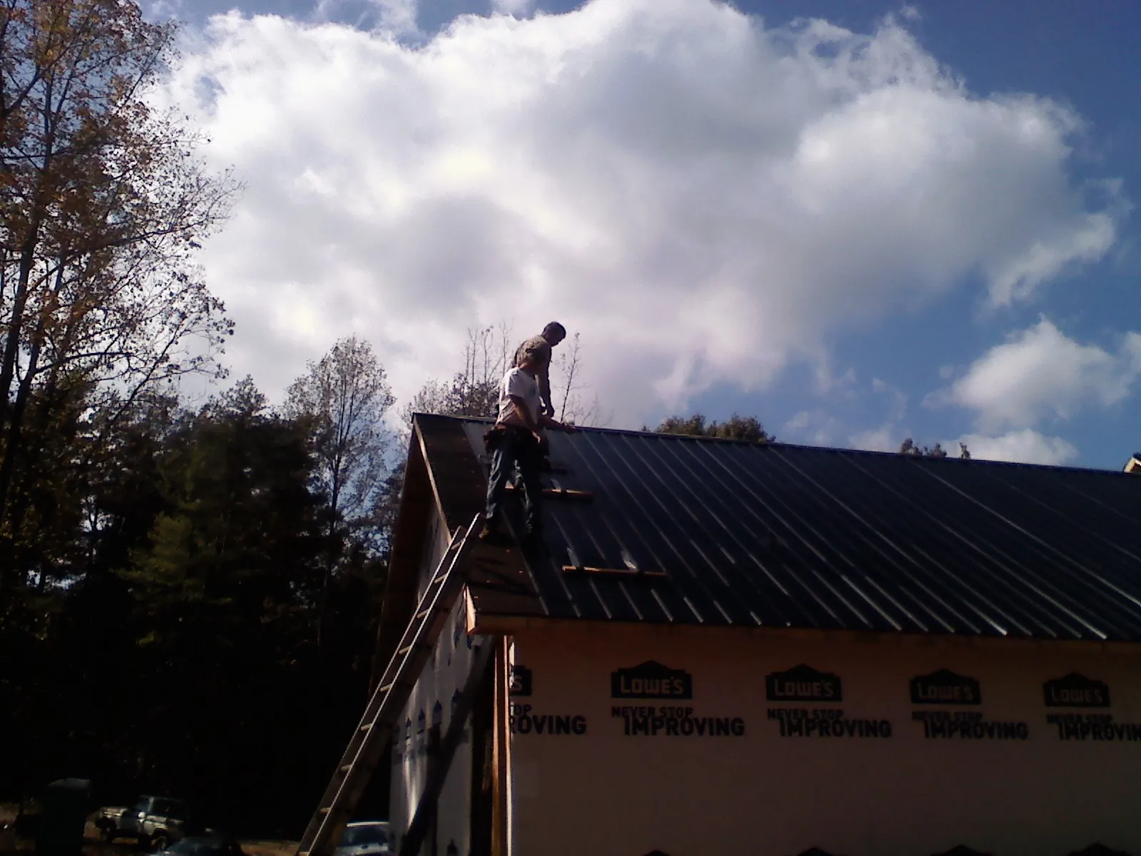 Roofer fastening dark metal panels high against a cloudy sky, from a Roof Inspection job in Truesdale