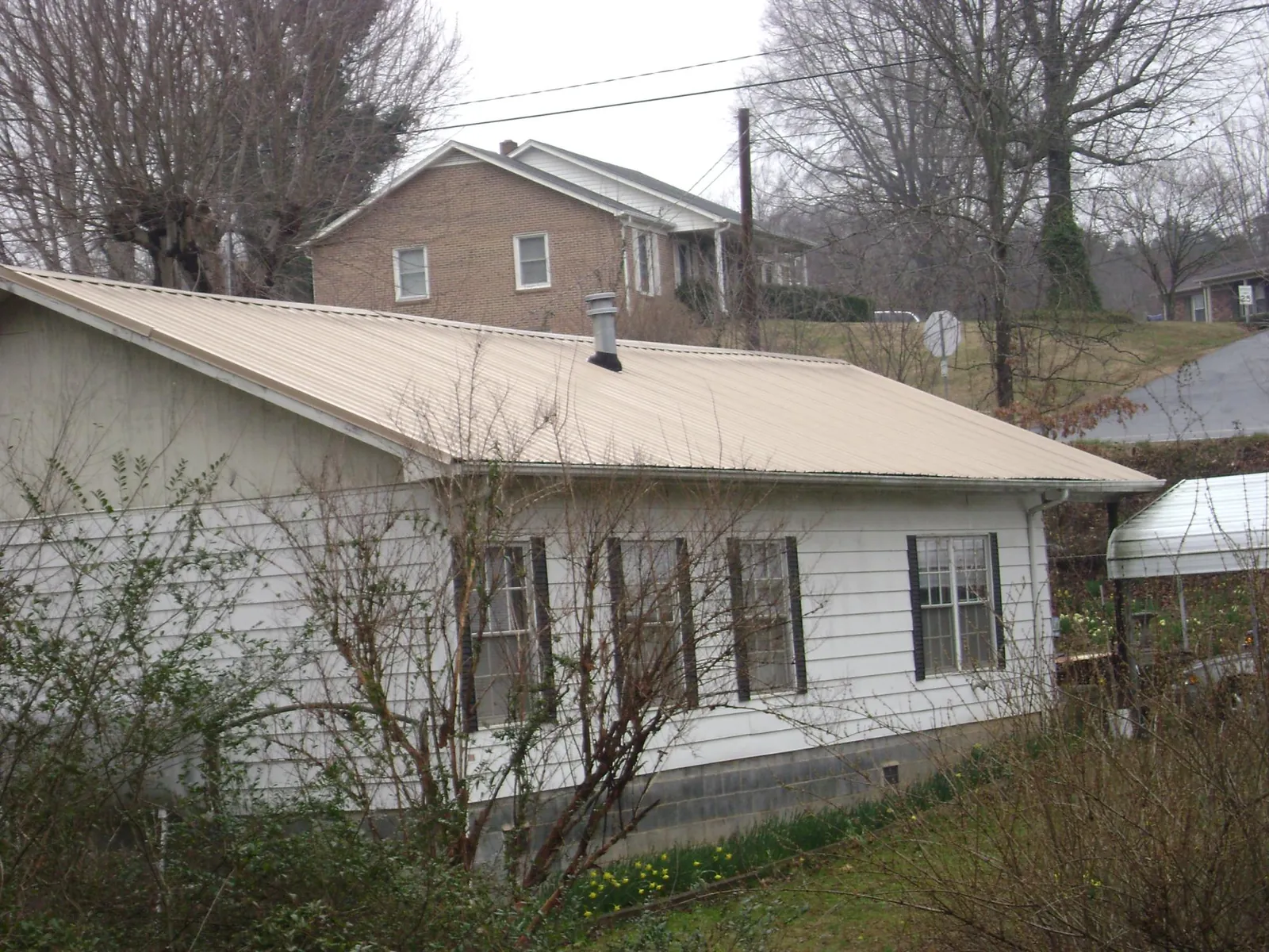 Tan metal roof on a white sided house set into a hillside — Commercial Roofing by Roofing Brothers in Truesdale